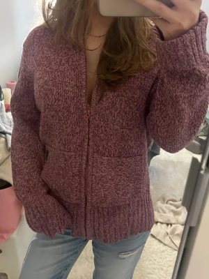 Rosa melerad ziptröja med fickor - Mysig rosa melerad ziptröja med två stora fickor framtill och ribbade muddar. Tröjan har en avslappnad passform och dragkedja hela vägen upp. Perfekt för lager på lager och chill dagar. 