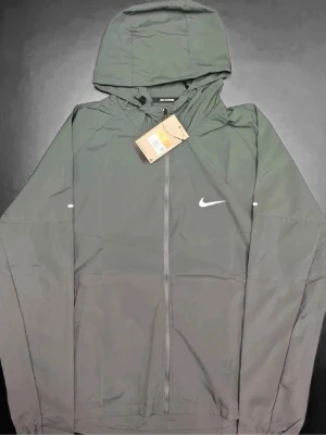 Nike Windbreaker jacket - Grå Nike windbreaker i storlek M helt ny i sin förpackning. Perfekt till träning eller vardagsstil.