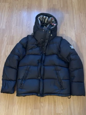 Svart pufferjacka från Burberry - Säljer en svart pufferjacka från Burberry, den är perfekt för vinter och sommar. Man kan göra den till både väst och en vanlig jacka. Säljer den på grund av att den inte passar mig. problemet med jackan är att den har små hål som du ser i bilden