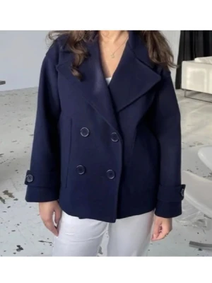 Mörkblå skepparkavaj med dubbelknäppning - Stilren mörkblå skepparkavaj med bred krage och dubbelknäppning framtill. Jackan har dekorativa knappar på ärmsluten och en rak, något boxig passform. Perfekt för dig som vill ha en klassisk och trendig look. 