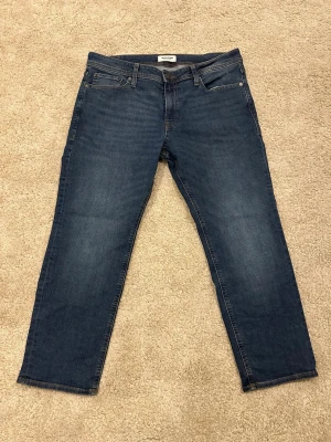 Mörkblå raka jeans från Jack & Jones - Snygga mörkblå jeans från Jack & Jones med klassisk femficksdesign och raka ben. Jeansen har en enkel look med diskreta sömmar och läderpatch bak i midjan. Perfekta för en stilren vardagsoutfit.