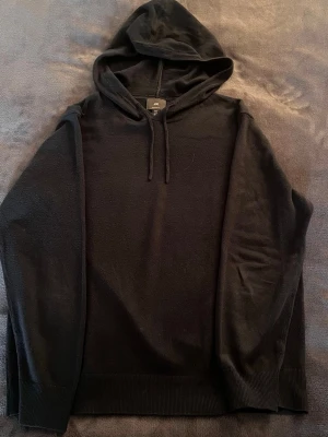 Svart hoodie från H&M - En stilren mörk blå hoodie från H&M med huva och dragsnören. Hoodien har långa ärmar och ribbade muddar vid ärmslut och nederkant. Tillverkad i mjukt material som känns skönt mot huden. Perfekt för en avslappnad look.