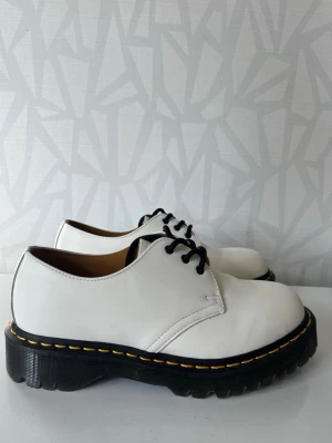Vita Dr. Martens loafers med snörning 1461 BEX - Säljer ett par vita Dr. Martens loafers med klassisk svart sula och gula sömmar. Skorna har svarta snören och är tillverkade i skinn. Perfekta för dig som vill ha en chunky och stilren look.Använd 1 gång!  📦Skickas snabbt ✨Mycket bra skick 📏Storlek 39 💸 Ordinarie pris 2375 kr 