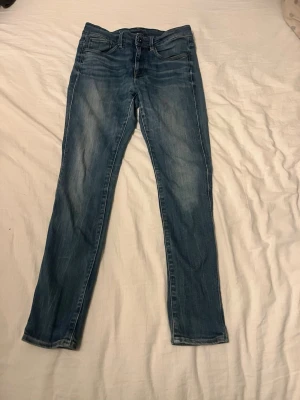 Blå slim fit jeans med slitningar - Säljer ett par blå slim fit jeans med snygga slitningar och tvättade detaljer. Jeansen har klassisk femficksdesign, normal midja och dragkedja med knapp. Perfekta för en avslappnad och trendig look.