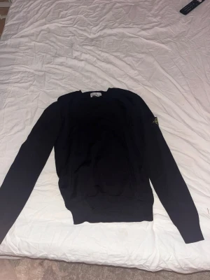 Stone Island tröja - Svart stickad tröja från Stone Island med klassisk rund halsringning och ikonisk logotyp-patch på ärmen. Tröjan har lång ärm och är tillverkad i ett mjukt, stickat material som passar perfekt till en stilren och avslappnad look. Storlek 152cm och den är lite kort i ärmarna på mig som är 169cm lång! Mycket bra skick skulle jag säga och nypriset när jag köpte den låg på 2000kr från farfetch 😁