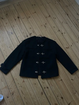 Svart jacka med spännen - Svart jacka med unika metallspännen framtill istället för vanliga knappar. Passar till många olika outfits.