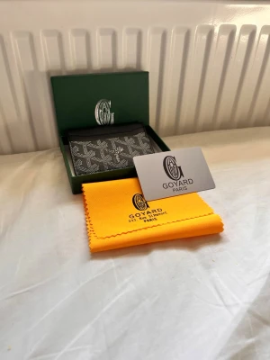 Svart kortfodral från G - Säljer ett stilrent svart kortfodral från G med det klassiska vita G-mönstret. Kortfodralet är tillverkat i canvas och har flera fack för kort. Kommer med original ask, gul putsduk och G-kort. Perfekt för dig som vill ha något exklusivt och snyggt i fickan.