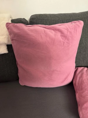 Stor rosa kudde i bomullstyg - En stor, fyrkantig kudde med rosa. Kudden har en enkel och stilren design som passar perfekt som dekoration i soffan eller sängen. Mjuk och bekväm att luta sig mot.