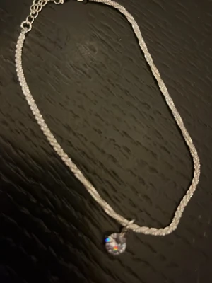 Silver armband/fotlänk med glittrande hänge - Säljer ett stilrent silverfärgat armband/fotlänk med ett gnistrande, rundslipat hänge. Kedjan är tunn och elegant med justerbar längd. Perfekt för dig som gillar enkla men snygga accessoarer. Materialet ser ut att vara metall med ett kristalliknande hänge.