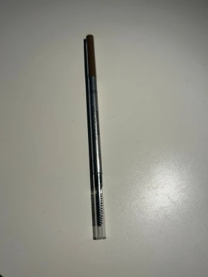 Maybelline ögonbrynspenna Blonde - En smidig ögonbrynspenna från Maybelline i färgen Blonde. Pennan har en ljusbrun nyans och kommer med en inbyggd borste i ena änden för enkel applicering och styling av brynen. Perfekt för att skapa naturliga och definierade ögonbryn.