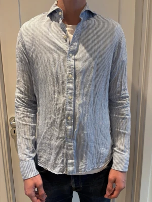 John Henric linneskjorta - Säljer en snygg ljusblå och vit randig skjorta från John Henric 100% linne i slim fit . Skjortan är använd enstaka gånger och säljs pga för liten. Inga defekter. 