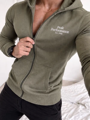 Olivgrön hoodie från Peak Performance 170 - Passar till S och M.    Snygg olivgrön hoodie med dragkedja från Peak Performance. Tryck på bröstet med logga och årtal. Utrustad med huva och två fickor framtill. Perfekt för en avslappnad och sportig stil.