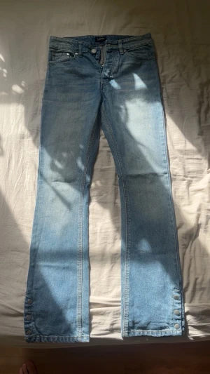 Ljusblå bootcut jeans med knappar (Storlek 30) - Snygga ljusblå bootcut jeans från BOOHOOMAN med klassisk femficksdesign och dekorativa knappar längs bensluten. Jeansen har normal midja och är tillverkade i denim.