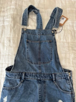 Hängslebyxor jeansshorts! - Blå Hängslebyxor jeans shorts som köptes nyligen från Sellpy men var försmå.☀️ Står storlek 38/M men jag skulle uppskatta de som en 34/36 S.🤗 Ursprunliga märket är pull&bear. 🥰Dom är perfekt nu inför sommaren för en cottage core cute outfitt eller något helt annan stil.