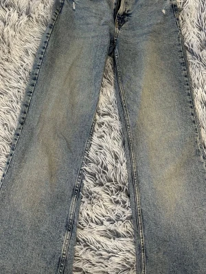 Blå raka jeans med  - Ett par klassiska blå jeans med raka ben och lätt slitna detaljer framtill, midmidja. Jeansen har en vintage tvätt och två bakfickor. Perfekta för en avslappnad och trendig look. 