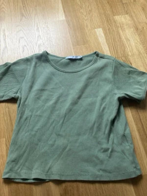 Ribbad grön kortärmad topp - En stilren ribbad topp i ljusgrön färg med rund halsringning och korta ärmar. Perfekt för en avslappnad look och enkel att matcha med jeans eller kjol. Mjuk och bekväm känsla.