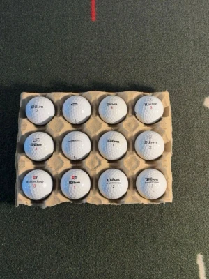 12 Wilson golfbollar  - Ett set med 12 vita golfbollar från Wilson, levererade i en kartongbricka. Bollarna har klassisk dimple-design och märkning med Wilson-logga samt olika nummer. Perfekt för golfentusiasten som vill fylla på med extra bollar.