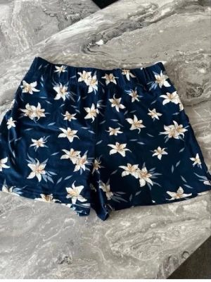 Blommiga marinblå shorts med resår storlek s/m - Snygga marinblå shorts med vitt blommönster och elastisk midja. Perfekta för varma dagar och har en avslappnad passform. Tillverkade i mjukt material som känns skönt mot huden.