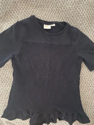 Mörkblå topp med volang från Gina Tricot - Supersöt mörkblå topp från Gina Tricot med smockad framsida och volangkant nedtill. 