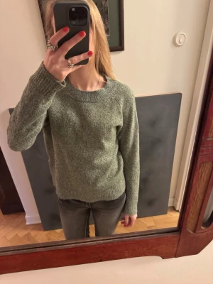 Grön stickad tröja - Mysig grön stickad tröja med rund halsringning och långa ärmar. Tröjan har en enkel, klassisk design med ribbstickade muddar vid ärmslut och nederkant. Perfekt för lager på lager och passar till jeans eller kjol. 