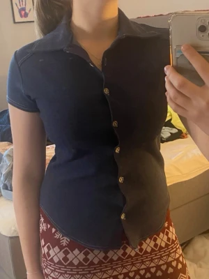 Mörkblå kortärmad skjorta/topp  - Snygg mörkblå skjorta med korta ärmar och knappar framtill. Skjortan har en figurnära passform och klassisk krage. Perfekt för en stilren look. Tror att storleken är S. Stretchig. 