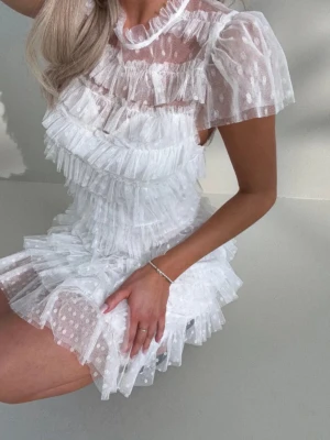 Vit volangklänning med prickar - Supersöt vit kortklänning med flera lager volanger och diskret prickigt mönster. Klänningen har korta ärmar i transparent tyg och rund halsringning. Perfekt för dig som vill sticka ut med en lekfull och romantisk look. Köpt på bubbleroom. Helt ny med prislapp, aldrig använd 🌸