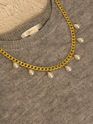 Guldfärgat halsband med pärldroppar - Snyggt halsband guldfärgad rostfritt stål kedja och hängande droppformade pärlor. Perfekt för att ge din outfit en trendig och elegant touch. Kedjan har en chunky design och pärlorna är vita och glansiga.