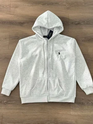 Ljusgrå hoodie från Polo Ralph Lauren - Snygg ljusgrå hoodie med dragkedja från Polo Ralph Lauren. Klassisk design med huva, dragsnören och kängurufickor. Liten broderad logga på bröstet. Perfekt för en avslappnad och stilren look.