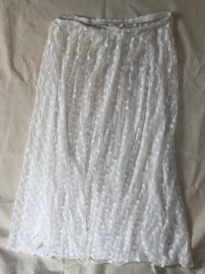 Vit meshkjol med blommönster - Säljer en vit, vadlång meshkjol med broderade små blommor. Kjolen har resår i midjan och är lätt transparent med ett romantiskt och luftigt uttryck. Perfekt för dig som gillar en feminin och trendig stil.