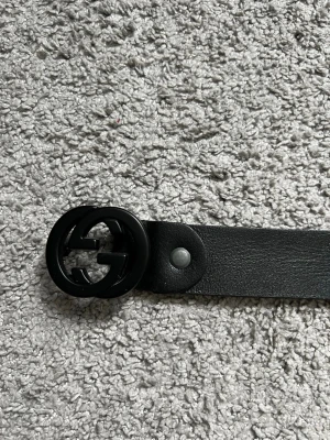 Svart bälte - Stilrent svart bälte. Bältet är gjort i slätt skinn och har en rundad form på spännet som ger en modern look. Perfekt accessoar för att lyfta din outfit.