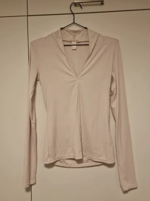 Ljusbeige långärmad topp med v-ringning - Säljer en ljusbeige långärmad topp med djup v-ringning och lätt rynkdetalj framtill. Toppen har en figurnära passform och är tillverkad i ett mjukt, stretchigt material. Perfekt att styla med jeans eller kjol för en trendig look.