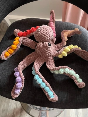 Virkad bläckfisk i pastellfärger - Handgjord virkad bläckfisk i mjukt sammetsgarn med åtta armar i olika pastellfärger. Kroppen är beige och armarna har inslag av lila, blått, gult, orange och rött. Säkerhetsögon. Perfekt som dekoration eller gosedjur.