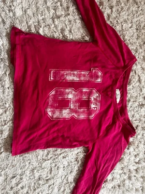 Mörkrosa långärmad topp A&F - Cool mörkrosa långärmad topp från Abercrombie & Fitch med stort tryck av siffran 18 framtill. Varan har märken av slitage på kragen och ärmarna. 