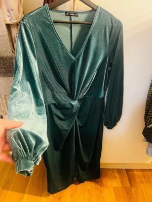 Grön manchesterklänning från SHEIN - Snygg grön klänning i manchester från SHEIN med v-ringning, långärmade puffärmar och twistad detalj framtill. Klänningen har en elegant midilängd och passar perfekt för dig som vill sticka ut med en cool textur och trendig färg.