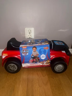 Paw Patrol röd sparkbil Marshall - Säljer en röd sparkbil från Paw Patrol med Marshall-tema. Bilen har svarta hjul, svart sits och detaljer i gult och vitt. Perfekt för yngre barn som gillar att köra runt inomhus. Gjord i plast och har roliga Paw Patrol-dekaler.