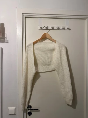 Vit stickad bolero - Kort, vit stickad bolero med lång ärm och öppen front. Perfekt att slänga över en topp eller klänning för extra värme och stil. Mjuk och stretchig stickning som ger en avslappnad men trendig look.