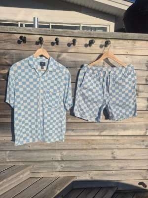 Blårutig kortärmad skjorta med tillhörande shorts strl SH&M - Kortärmad skjorta med tillhörande shorts frå H&M. Aldrig använt, endast sköljts upp och hängt i garderoben. Dvs absolut nyskick! 