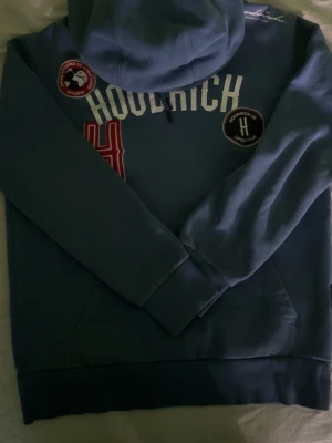 Blå hoodie från Hoodrich med patches - Snygg blå hoodie från Hoodrich med flera patches och broderade detaljer på bröstet. Stor vit logga framtill, röd patch och svart rund patch ger en streetwear vibe. Klassisk huva och ribbade muddar. Perfekt för dig som gillar urban stil.