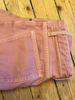 Ljusrosa vida byxor - Säljer ett par snygga rosa baggy byxor , vida ben och klassiska fickor både fram och bak. Byxorna har bälteshällor och stängs med knapp och dragkedja. Perfekta för dig som vill sticka ut med färg och mjukt material.