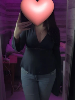 Mörkblå topp med spetsdetalj - Populär Snygg mörkblå topp med djup v-ringning och spetsdetalj i midjan. Blusen har långa ärmar och figurnära passform som framhäver midjan. Perfekt att styla med jeans eller kjol för en trendig look. Storlek S