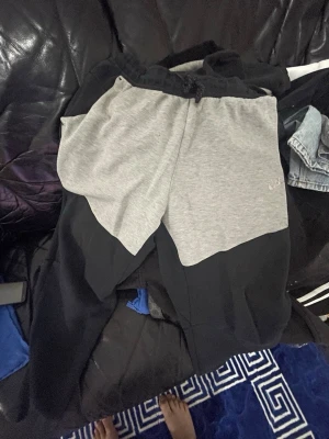 Tvåfärgade mjukisbyxor i svart och grå - Snygga mjukisbyxor med unik tvåfärgad design i svart och ljusgrått. Byxorna har resår i midjan och är tillverkade i mjukt material som passar perfekt för en avslappnad stil. Perfekta för chill eller streetwear.