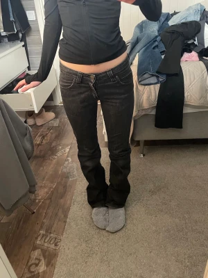 Svarta bootcut jeans med låg midja - Säljer ett par svarta bootcut jeans med låg midja och klassisk femficksdesign. Jeansen har en snygg tvätt och sitter tajt över låren för att sedan bli vidare nedtill. Perfekta för dig som gillar en retro och avslappnad stil.