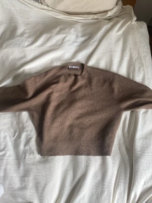 Brun stickad tröja från Zara - Mysig brun stickad tröja från Zara med rund halsringning och ribbade muddar vid ärmslut och nederkant. Tröjan har en enkel, klassisk design och är perfekt för lager på lager under kyliga dagar.