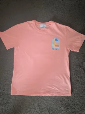 Casablanca rosa t-shirt  - Snygg rosa t-shirt från Casablanca med färgglatt tryck av ett fönster och texten 'Casa Blanca' på bröstet och ryggen. Klassisk passform och rund halsringning, perfekt för en avslappnad stil.