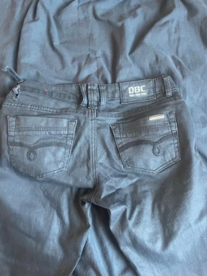 Svarta jeans från DBC - Snygga svarta jeans från DBC med klassisk femficksmodell och dekorativa sömmar på bakfickorna. Jeansen har bälteshällor och metallknappar. Passar perfekt till en avslappnad streetwear-look. OBS- de har en liten slitning vid bält hålet. Kontakta gärna ❤️