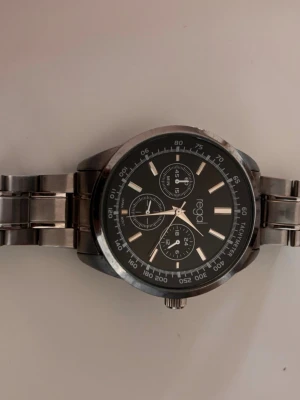 Regal silverfärgad klocka med länk - Stilren klocka från Regal med svart urtavla och silverfärgat armband i metall. Klockan har flera små urtavlor och tydliga markeringar. Perfekt accessoar för dig som gillar en klassisk och modern look.