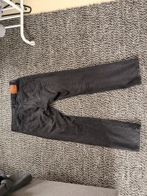 Svarta raka jeans från Levi's - Säljer ett par svarta jeans från Levi's med klassisk rak passform och femficksdesign. Jeansen har en läderpatch bak i midjan och är tillverkade i denim. Perfekta för en clean och stilren look.