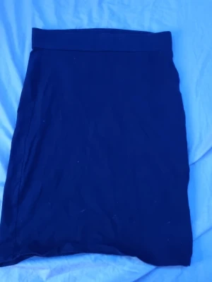 Svart kjol från 157 - Enkel och stilren svart kjol från 157 med rak passform och bred linning. Kjolen är perfekt för dig som gillar minimalistisk stil och passar till många olika outfits. Tillverkad i mjukt material som känns skönt mot huden.