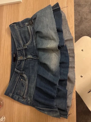 Blå jeanskjol med volang - Unik blå jeanskjol från Lee med volangdetalj i olika nyanser av denim. Kjolen har klassiska jeansfickor och knappstängning framtill. Perfekt för dig som gillar en kreativ och edgy stil.