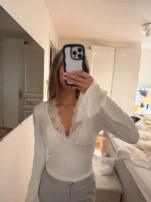 Vit långärmad topp med spets - Supersnygg vit långärmad topp med v-ringning och spetsdetaljer vid halsen. Ärmarna är vida och ger en trendig look. Står ingen storlek passa mig som bruka ha xs/s